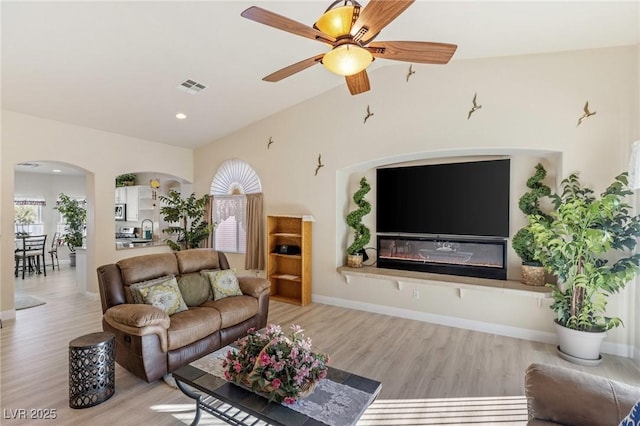 living room with ceiling fan, light wood-type flooring, lofted ceiling, and sink