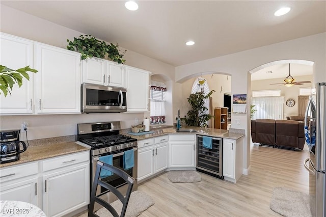 kitchen with stainless steel appliances, sink, white cabinetry, ceiling fan, and beverage cooler