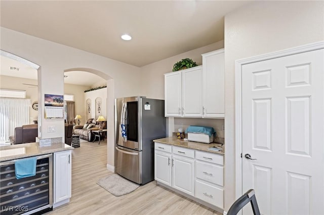 kitchen with light stone counters, beverage cooler, light wood-type flooring, white cabinetry, and stainless steel refrigerator