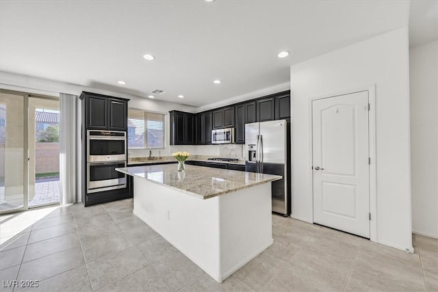 kitchen with stainless steel appliances, light stone countertops, light tile patterned floors, and a center island