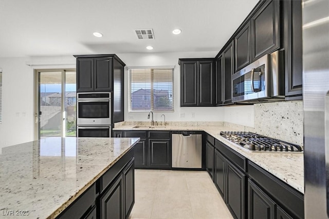 kitchen featuring sink, light tile patterned floors, decorative backsplash, light stone countertops, and appliances with stainless steel finishes