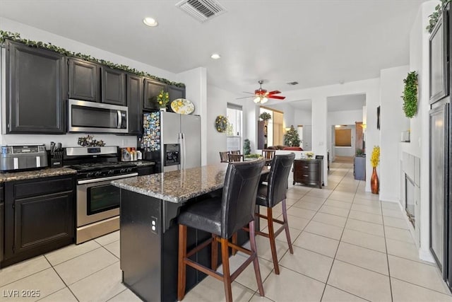 kitchen featuring a kitchen breakfast bar, dark stone countertops, stainless steel appliances, a center island, and ceiling fan