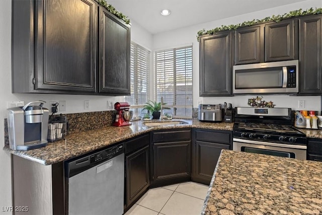 kitchen featuring dark stone countertops, appliances with stainless steel finishes, light tile patterned floors, sink, and dark brown cabinets