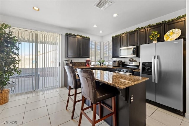 kitchen featuring a kitchen island, a breakfast bar area, appliances with stainless steel finishes, light tile patterned flooring, and dark brown cabinets