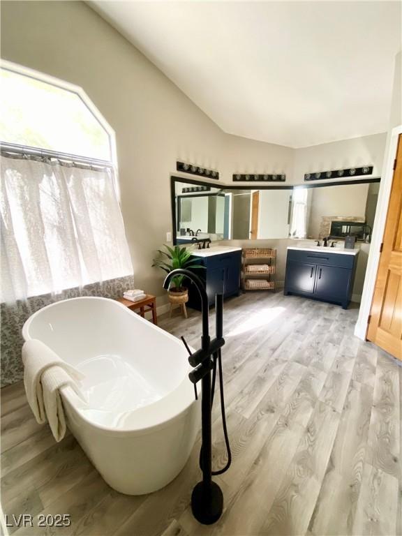 bathroom featuring a tub to relax in, vaulted ceiling, wood-type flooring, and vanity