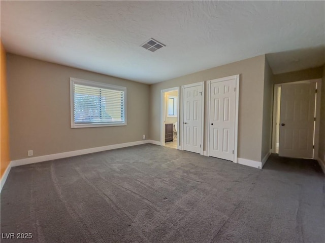 unfurnished bedroom featuring two closets, dark colored carpet, and connected bathroom