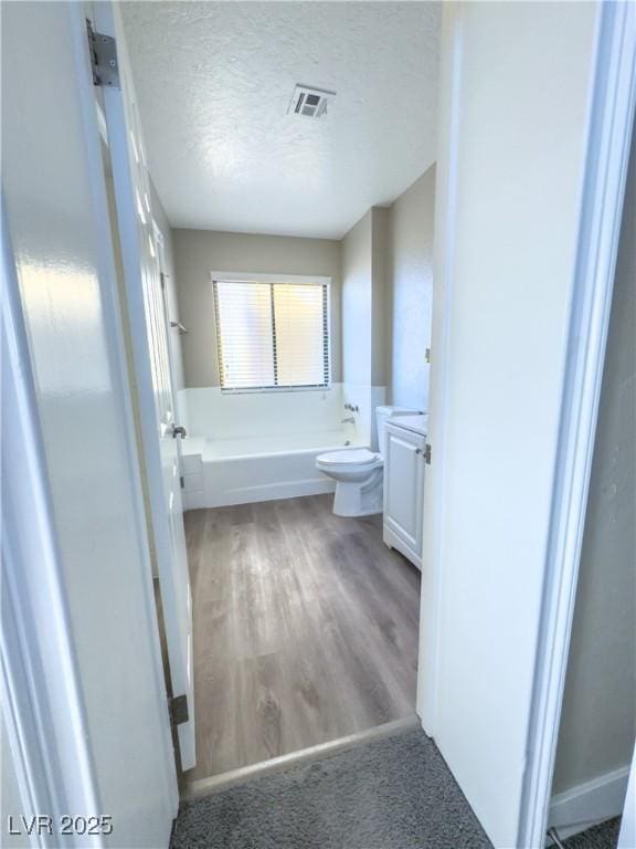 bathroom with a tub to relax in, wood-type flooring, toilet, vanity, and a textured ceiling