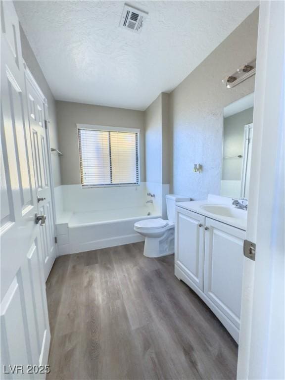 bathroom with a textured ceiling, a bath, hardwood / wood-style flooring, toilet, and vanity