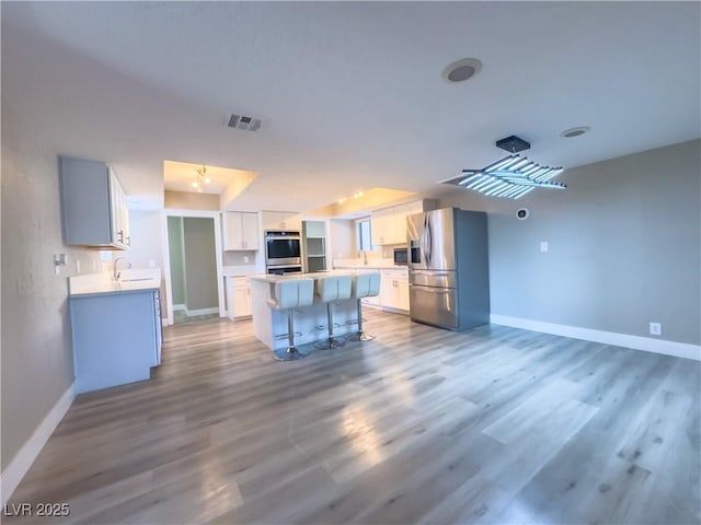 kitchen with a breakfast bar, hardwood / wood-style floors, a kitchen island, white cabinets, and appliances with stainless steel finishes