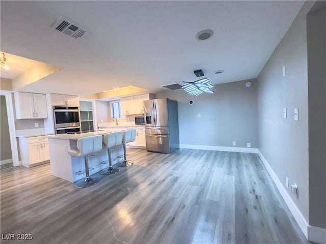 kitchen with a breakfast bar area, appliances with stainless steel finishes, light hardwood / wood-style floors, a center island, and white cabinetry