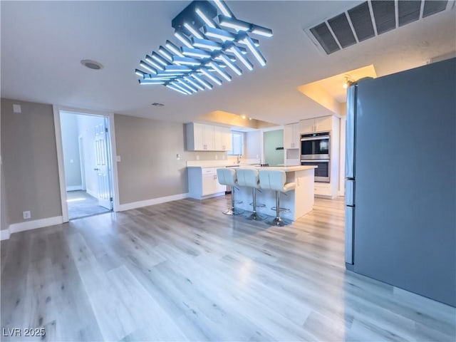 kitchen with a center island, stainless steel appliances, a breakfast bar, light wood-type flooring, and white cabinetry