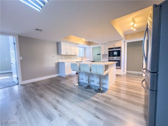 kitchen featuring stainless steel appliances, white cabinetry, a center island, a kitchen breakfast bar, and light hardwood / wood-style floors