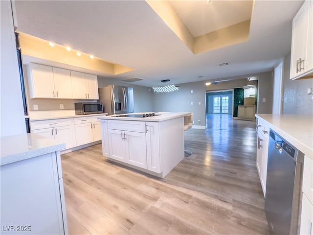 kitchen with white cabinets, appliances with stainless steel finishes, a tray ceiling, and a center island