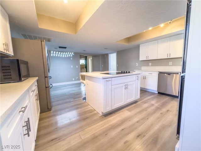 kitchen with a raised ceiling, black appliances, light hardwood / wood-style floors, a center island, and white cabinetry