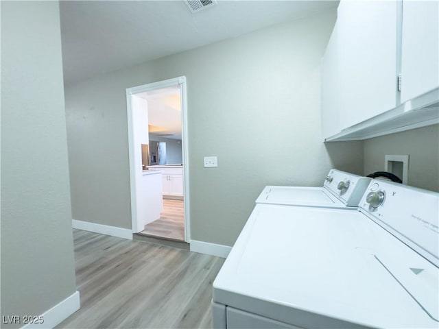 clothes washing area with washing machine and clothes dryer, light wood-type flooring, and cabinets