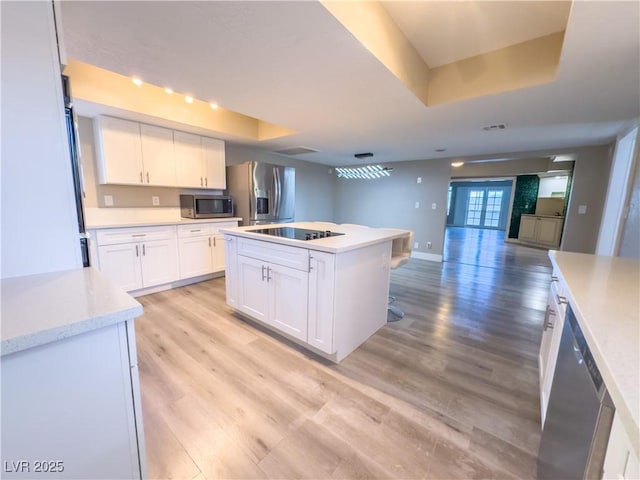 kitchen with white cabinets, appliances with stainless steel finishes, a tray ceiling, and a center island