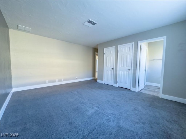 unfurnished bedroom with ensuite bathroom, two closets, and dark carpet