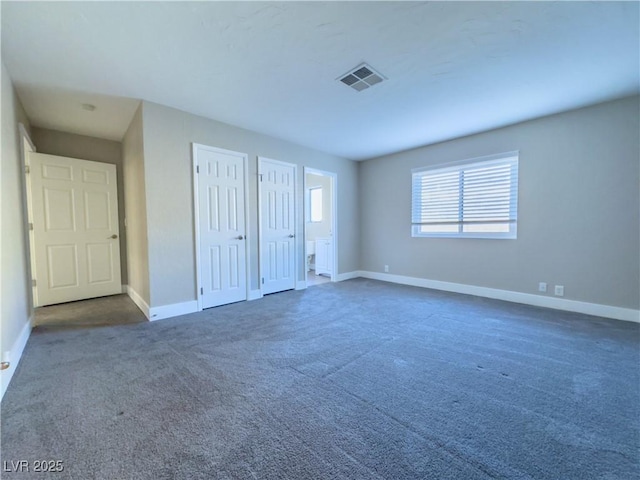 unfurnished bedroom featuring dark carpet and two closets