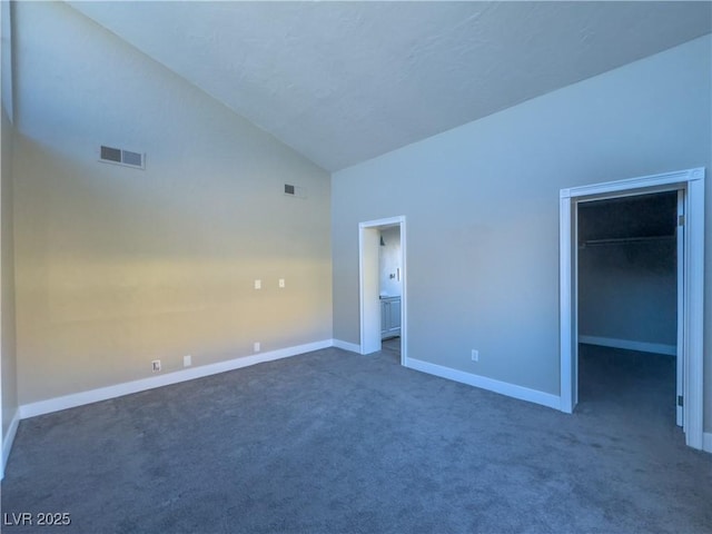 unfurnished bedroom featuring a spacious closet, a closet, high vaulted ceiling, and dark colored carpet