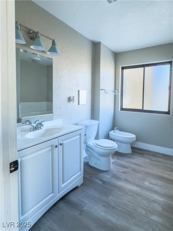 bathroom featuring toilet, wood-type flooring, vanity, and a bidet