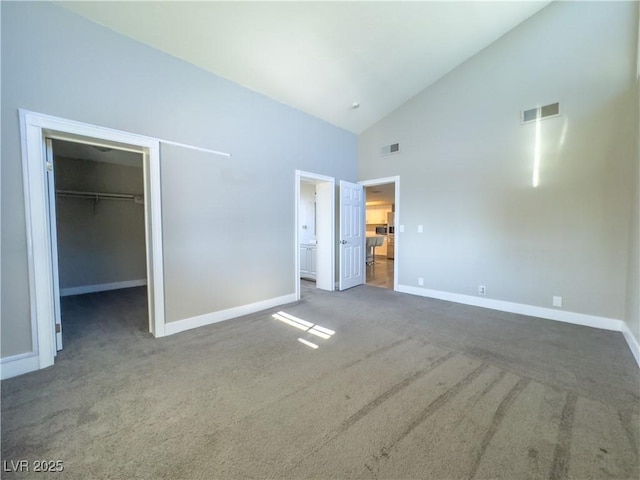 unfurnished bedroom featuring a closet, dark colored carpet, a spacious closet, high vaulted ceiling, and ensuite bathroom