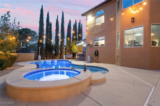 pool at dusk featuring an in ground hot tub, a patio area, and exterior bar