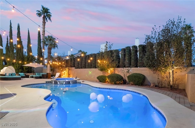 pool at dusk featuring an in ground hot tub and a patio area