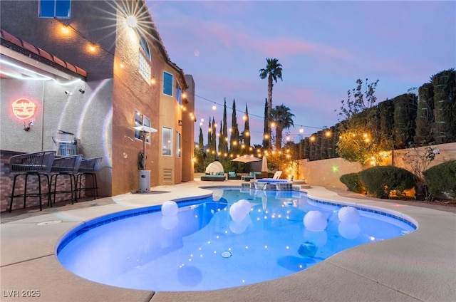 pool at dusk with a patio area, an in ground hot tub, and an outdoor bar