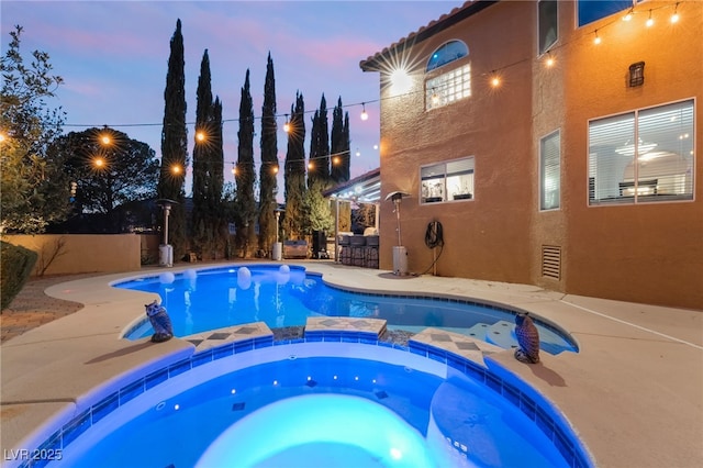 pool at dusk with a bar, a patio, and an in ground hot tub