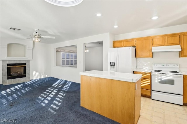 kitchen with tile countertops, ceiling fan, a tiled fireplace, white appliances, and a center island