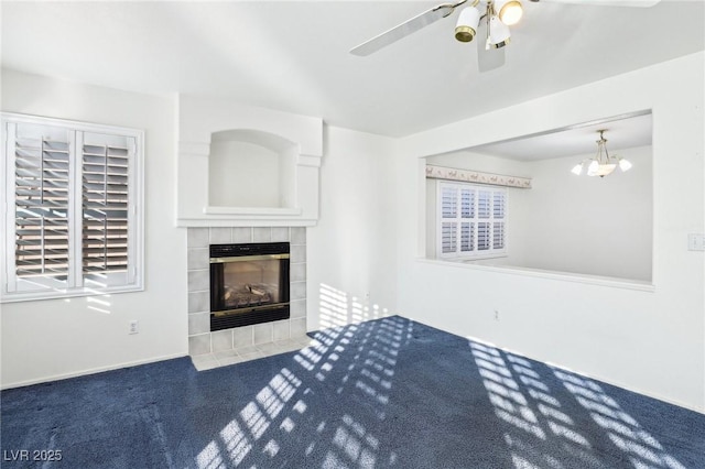 unfurnished living room with ceiling fan with notable chandelier, a tiled fireplace, and carpet flooring