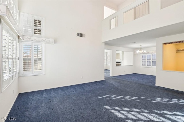 unfurnished living room with an inviting chandelier, a towering ceiling, and dark carpet