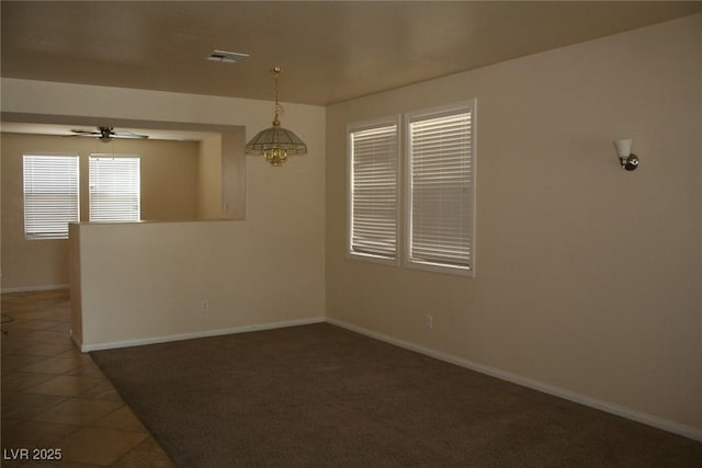 spare room featuring dark tile patterned floors and ceiling fan with notable chandelier