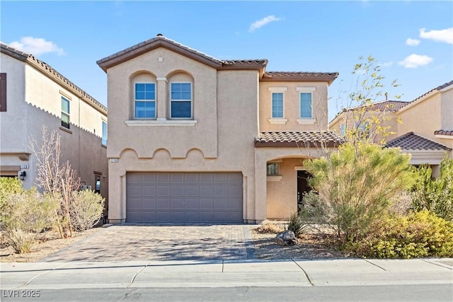 mediterranean / spanish house with an attached garage, a tiled roof, decorative driveway, and stucco siding