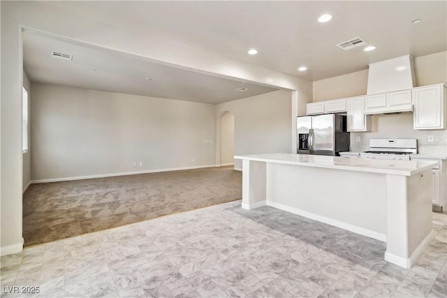 kitchen with a spacious island, stainless steel refrigerator with ice dispenser, white cabinetry, light carpet, and white range oven