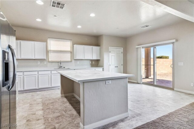 kitchen with stainless steel refrigerator with ice dispenser, sink, white cabinetry, and a center island