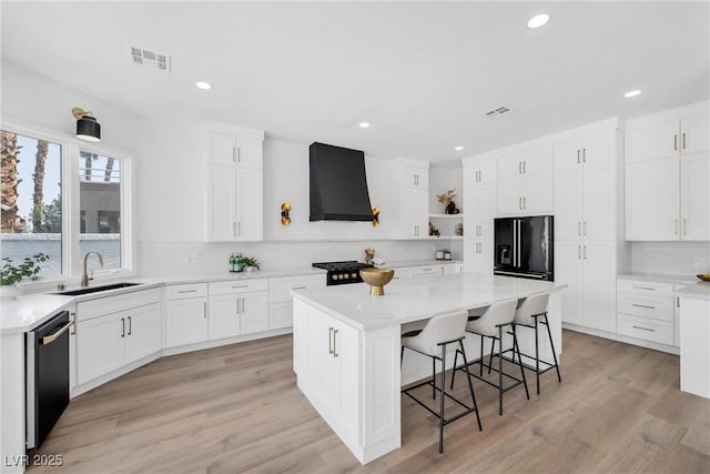 kitchen with a center island, wall chimney exhaust hood, black appliances, decorative backsplash, and sink