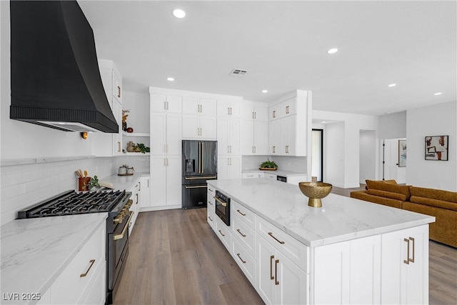 kitchen featuring black fridge, custom range hood, range with gas stovetop, light stone counters, and a center island