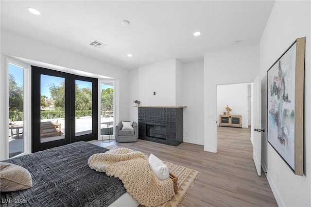 bedroom with light wood-type flooring, a brick fireplace, access to exterior, and french doors