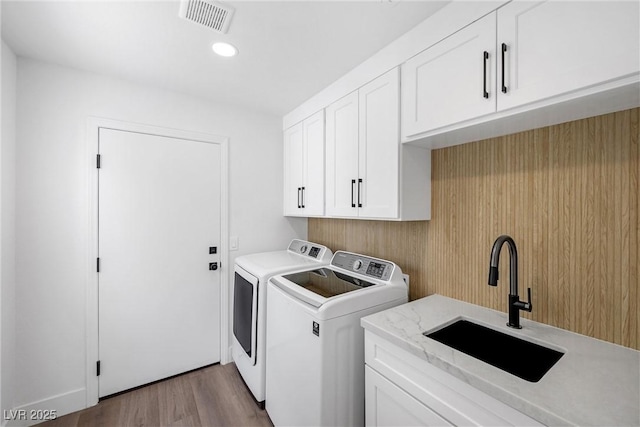 laundry room featuring cabinets, separate washer and dryer, light wood-type flooring, and sink