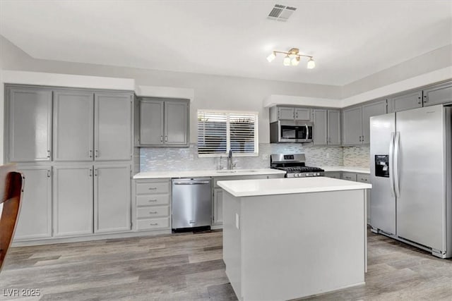 kitchen featuring stainless steel appliances, gray cabinetry, a center island, light wood-type flooring, and sink