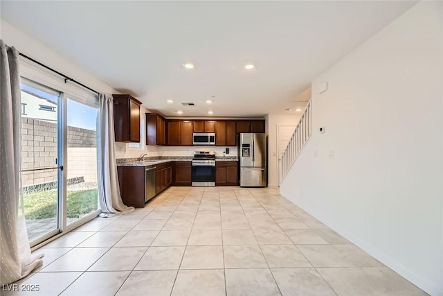 kitchen with appliances with stainless steel finishes, sink, light tile patterned flooring, light stone counters, and dark brown cabinets