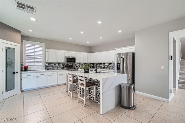 kitchen with white cabinetry, a kitchen bar, appliances with stainless steel finishes, a kitchen island with sink, and sink