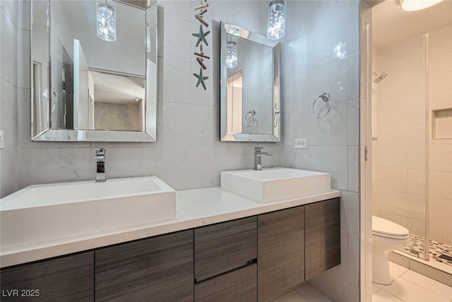 bathroom with toilet, vanity, tile walls, tile patterned floors, and a shower with door