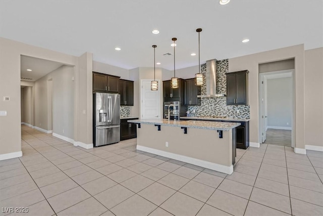 kitchen featuring wall chimney range hood, backsplash, stainless steel fridge with ice dispenser, light tile patterned floors, and a center island with sink