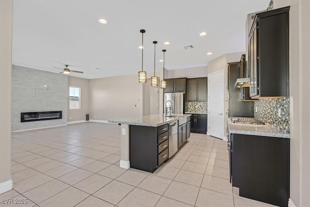 kitchen with an island with sink, ceiling fan, tasteful backsplash, decorative light fixtures, and light tile patterned flooring