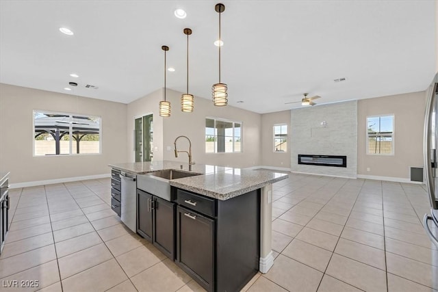 kitchen with decorative light fixtures, ceiling fan, sink, an island with sink, and light stone counters