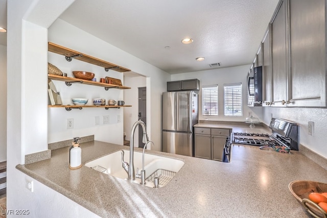 kitchen featuring a textured ceiling, stove, sink, and stainless steel refrigerator