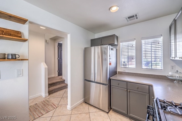 kitchen featuring light tile patterned floors, gray cabinetry, range, and stainless steel refrigerator