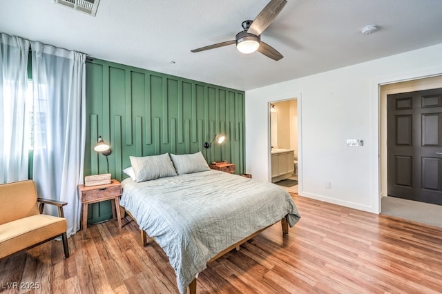 bedroom with light wood-type flooring, ceiling fan, ensuite bathroom, and a textured ceiling